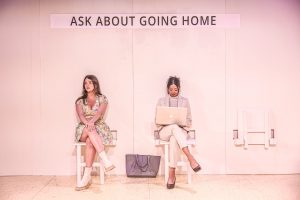 Tow women sitting below a sign that reads: Ask about going home